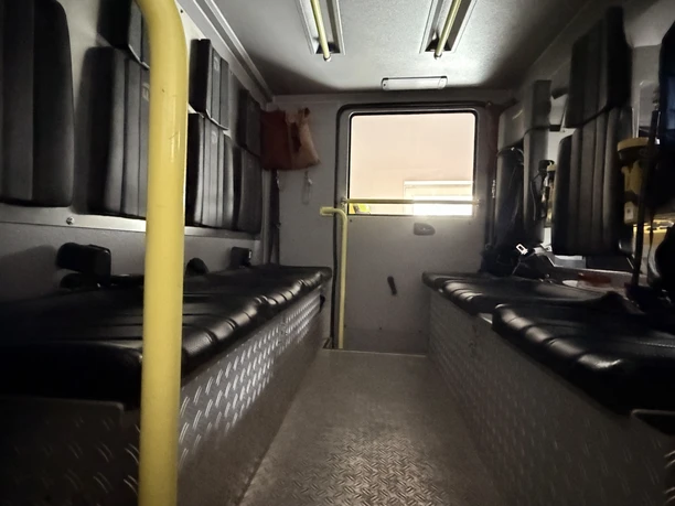 IMG_0803.jpg Innenraum eines Feuerwehrfahrzeugs mit gepolsterten Sitzbänken, Haltestangen und Ausrüstungen.