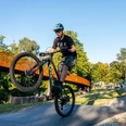 Area61 Mountainbiker hebt Vorderrad auf Pumptrack, weitere Fahrer und Fußgänger im Hintergrund