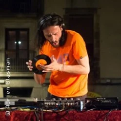 Ein DJ mit Kopfhörern hält eine kleine Schallplatte über einem beleuchteten Mischpult.
