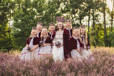 2026-01-Heideblütenfest-Amelinghausen.jpg Heidekönigin mit Heideprinzessinnen in traditionellen Kleidern zwischen blühender Heide sitzend.