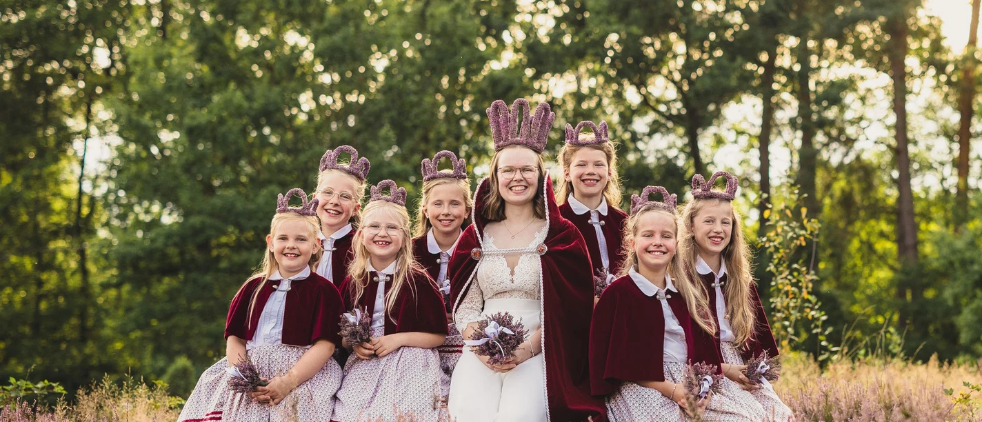 2026-01-Heideblütenfest-Amelinghausen.jpg Heidekönigin mit Heideprinzessinnen in traditionellen Kleidern zwischen blühender Heide sitzend.
