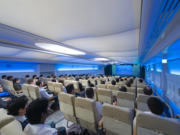 The Aircraft at Burghof - Event hall Modern event hall in airplane design with blue lighting and audience in beige airplane seats.