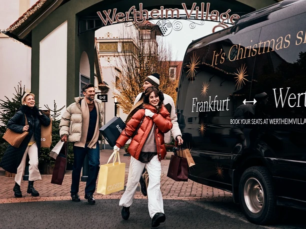 Wertheim Village - Shopping-Erlebnis Shopping-Gruppe mit Tüten vor dem Eingang von Wertheim Village.