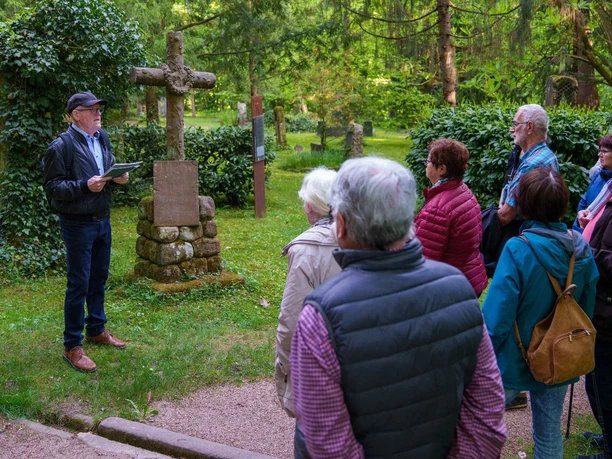 Gruppe hört dem Gästeführer zu, der vor einem Steinkreuz seinen Vortrag hält