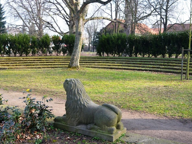 Salzgitter-Flachstoeckheim_Freilichtbuehne_HD_16zu9.JPG Steinerne Löwenfigur vor halbrunder Freilichtbühne mit Rasenstufen und alten Bäumen im Gutspark.