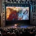 Bach in Space Pianist in front of a large space motif on the stage of a packed concert hall