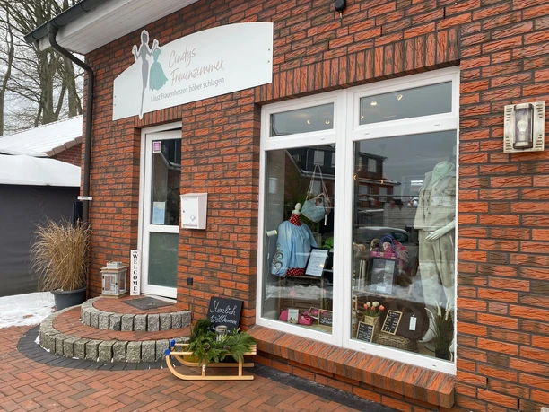 Cindys-frauenzimmer-bispingen-außenansicht.jpg Eingang eines Modegeschäfts mit Schaufenster, Kleidung, Dekoration und winterlicher Außendeko.