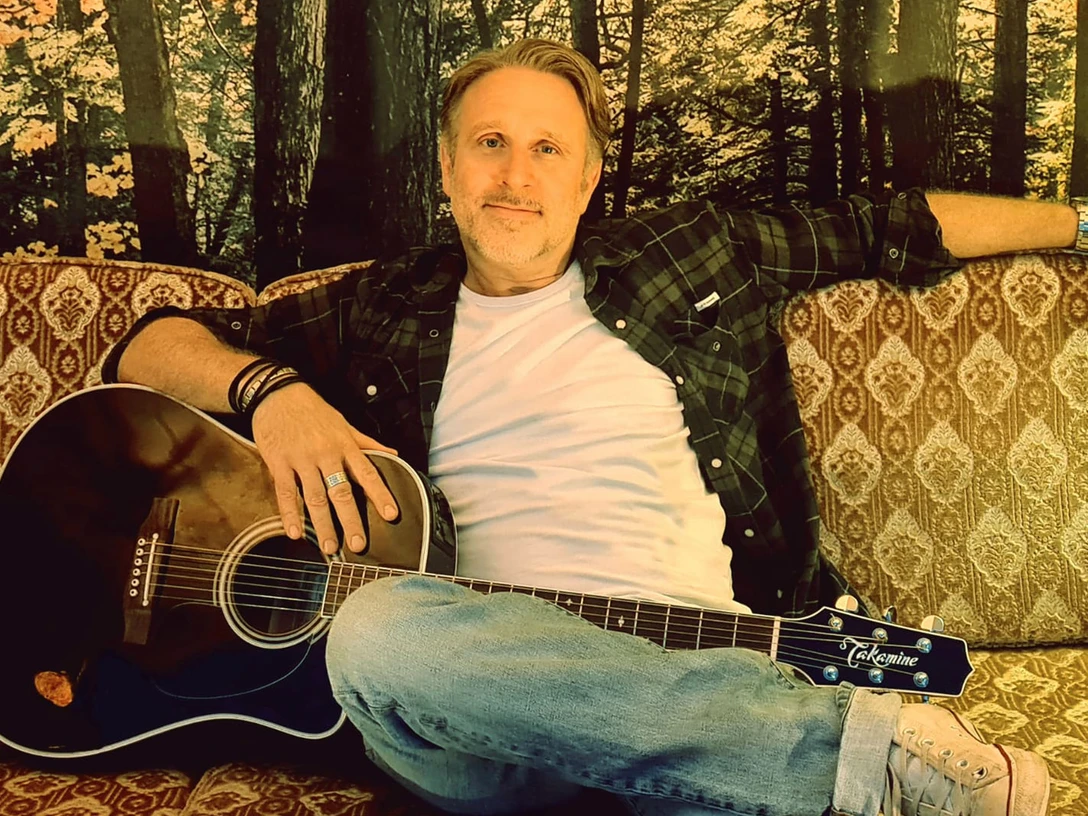 Jason Foley.jpg Ein Mann auf einem Sofa mit Gitarre.