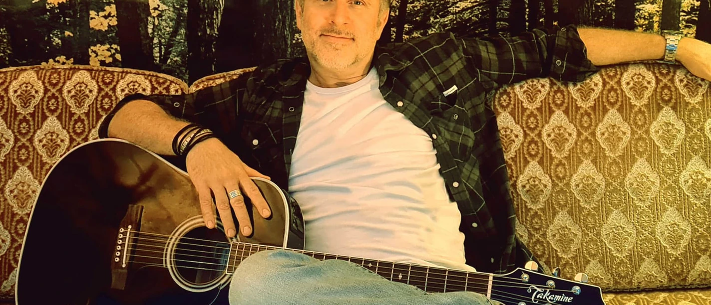 Jason Foley.jpg Ein Mann auf einem Sofa mit Gitarre.