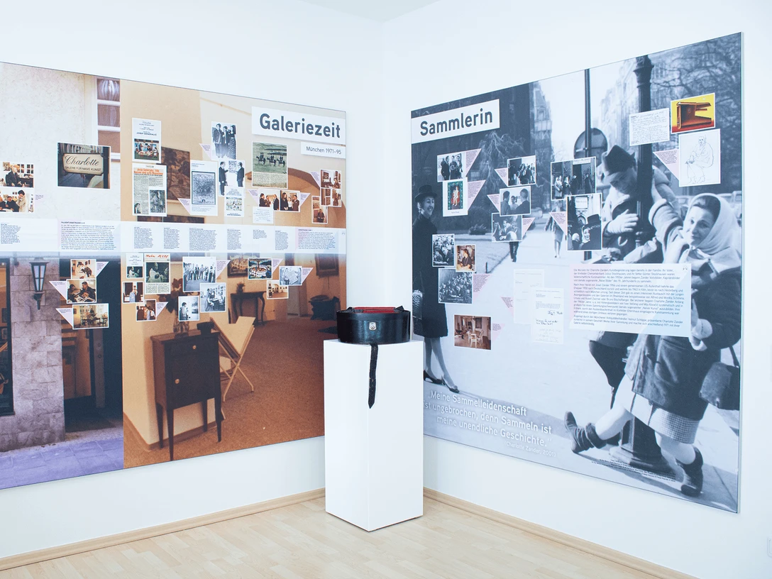 Exhibition room at ZADIK Ausstellungsraum mit zwei bebilderten Wandtafeln und einem Podest mit Tasche.Exhibition room with two illustrated wall panels and a pedestal with bag.