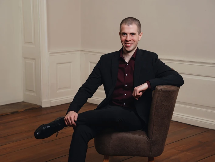 buesum-Sänger Markus 2560x1707.jpeg Ein Mann im schwarzen Anzug auf einem Sessel vor einer weißen Wand.