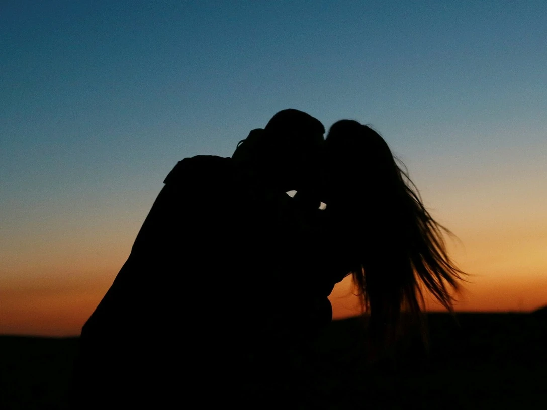 Paarzeit Ein Paar umarmt sich im Abendlicht, der Himmel leuchtet in warmen Farben des Sonnenuntergangs.