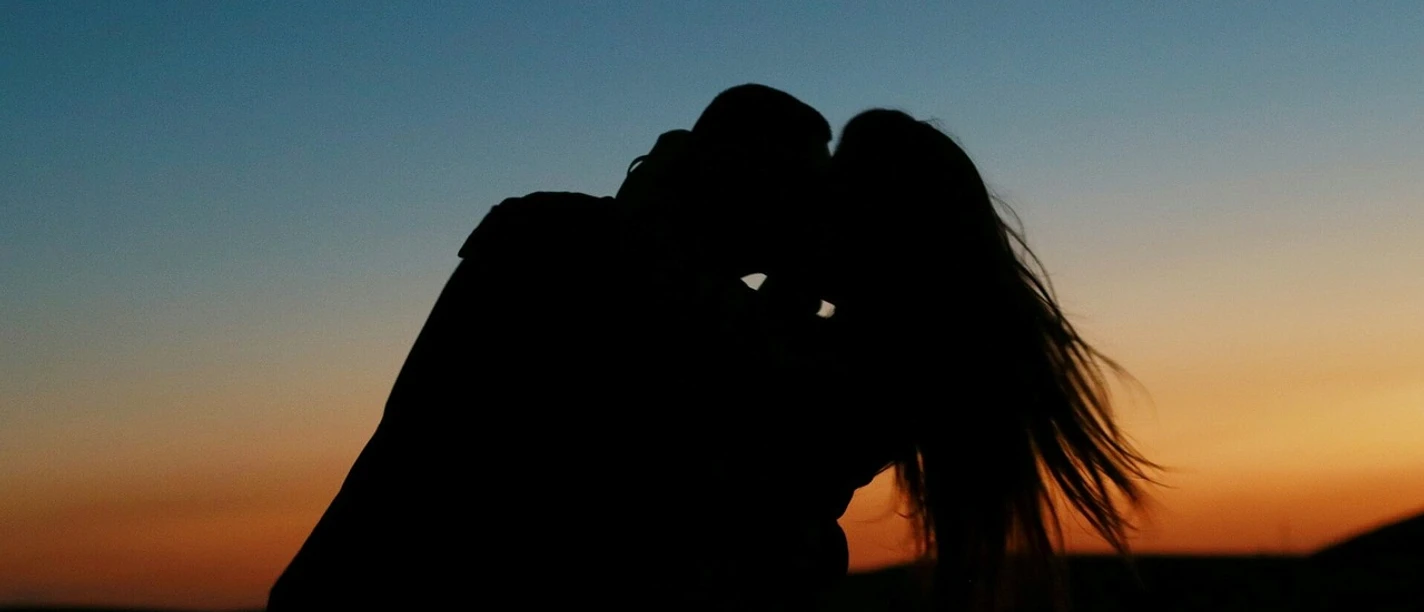 Paarzeit Ein Paar umarmt sich im Abendlicht, der Himmel leuchtet in warmen Farben des Sonnenuntergangs.