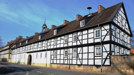 Gutshof_Flachstöckheim (2)_HD_16zu9.JPG Langgestrecktes Fachwerkgebäude mit Torbogen, dunklem Gebälk und roten Ziegeldächern unter blauem Himmel.