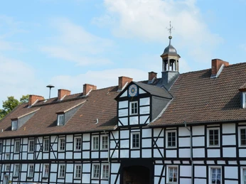 Gutshof_Flachstöckheim (14)_HD_16zu9.JPG Historisches Fachwerkgebäude mit rotem Ziegeldach und Turmaufbau unter blauem Himmel.