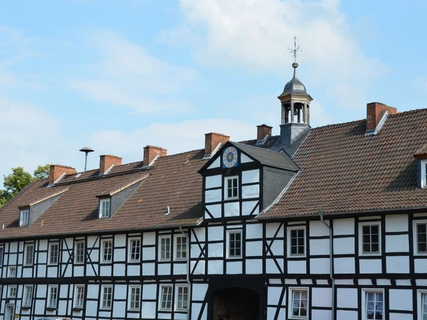 Gutshof_Flachstöckheim (14)_HD_16zu9.JPG Historisches Fachwerkgebäude mit rotem Ziegeldach und Turmaufbau unter blauem Himmel.