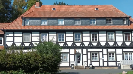 Gutshof_Flachstöckheim (21)_HD_16zu9.jpg Zweigeschossiges Fachwerkhaus mit rotem Ziegeldach und weißen Gefachen unter blauem Himmel.