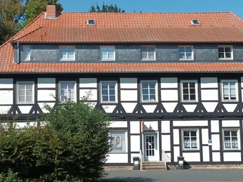 Gutshof_Flachstöckheim (21)_HD_16zu9.jpg Zweigeschossiges Fachwerkhaus mit rotem Ziegeldach und weißen Gefachen unter blauem Himmel.