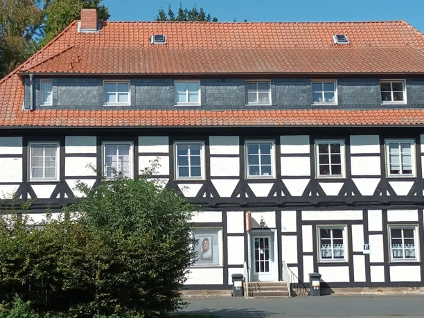 Gutshof_Flachstöckheim (21)_HD_16zu9.jpg Zweigeschossiges Fachwerkhaus mit rotem Ziegeldach und weißen Gefachen unter blauem Himmel.