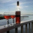 Roséwein und zwei Gläser bei tiefstehender Sonne am Meer Zwei Gläser Roséwein und eine Flasche auf einem Geländer mit Blick auf den See im Abendlicht