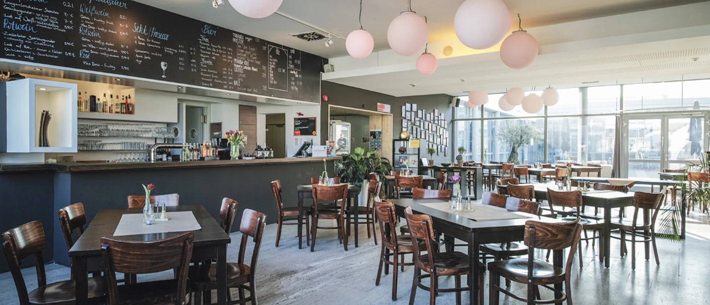 LIDO®Thomas Kubiczek.jpg Helles Restaurant mit Holztischen und runden Lampen im LIDO.