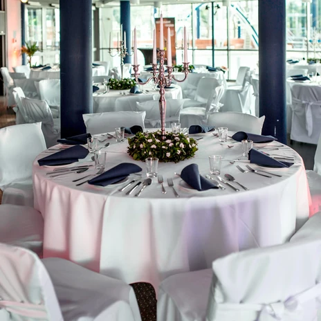 hallenbad 11.jpg Runder Tisch mit weiĂźer Tischdecke, Besteck, blauen Servietten und Kerzenleuchter in festlichem Raum.