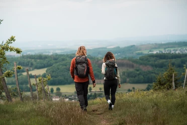 Wandern an der Nordhelle Zwei Wandernde mit Rucksäcken auf Wiesenpfad mit weitem Blick über das Sauerland