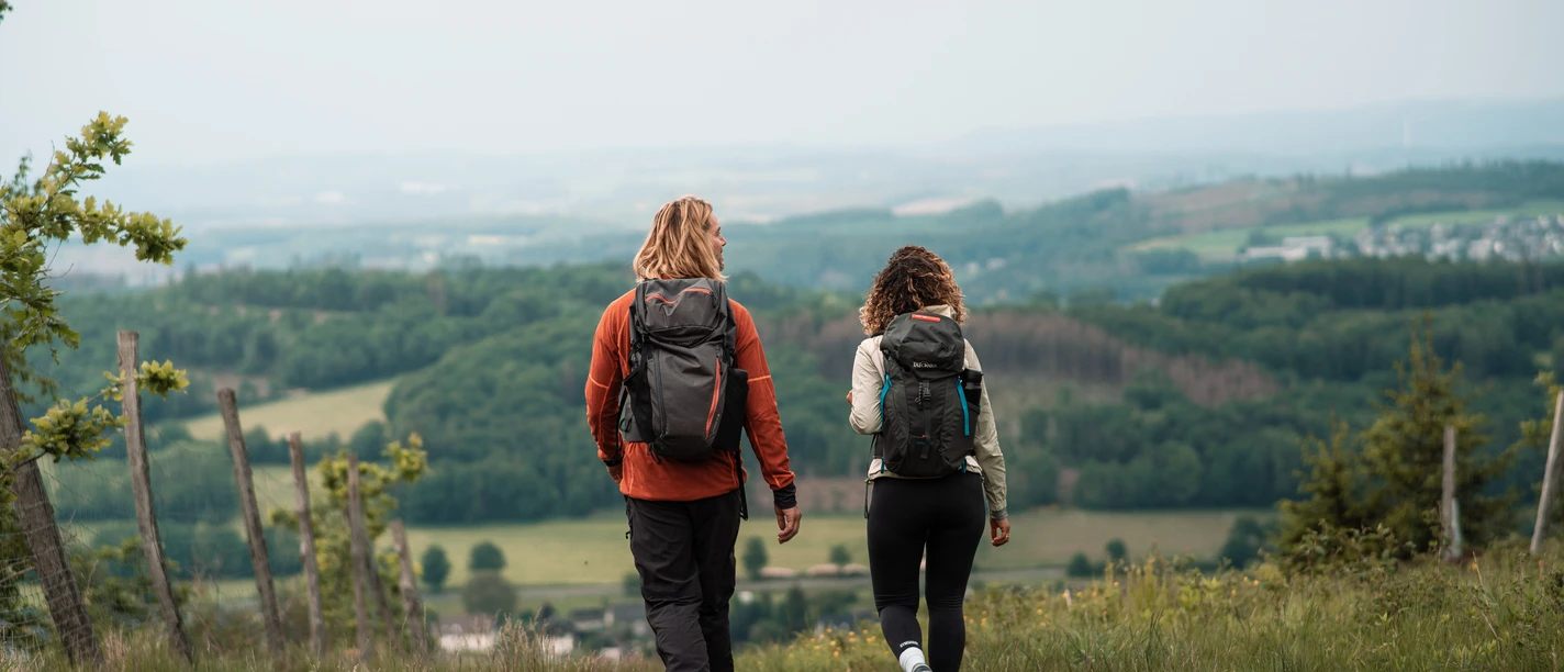 Zwei Wandernde mit Rucksäcken auf Wiesenpfad mit weitem Blick über das Sauerland