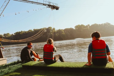 Wasserski und Wakeboard Neuhaus Menschen mit Schwimmwesten am See bereiten sich bei Sonnenschein auf Wasserski vor.