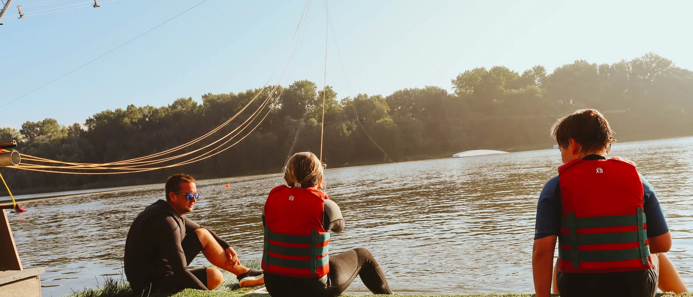 Wasserski und Wakeboard Neuhaus Menschen mit Schwimmwesten am See bereiten sich bei Sonnenschein auf Wasserski vor.