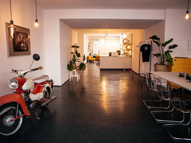 Eingang modern eingerichteter, langer Raum mit Tisch und Stühlen im Vordergrund und Loungemöbeln im Hintergrund