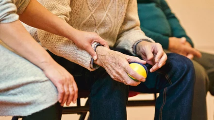 Bild Pflege Senioren.jpg Pflegekraft stützt behutsam den Arm eines älteren Menschen, der einen bunten Ball hält.