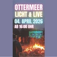 Ottermeer Licht&Live (1920x1080).jpg Menschen versammeln sich bei einem Lagerfeuer vor einer bunt beleuchteten Bühne am Ottermeer.