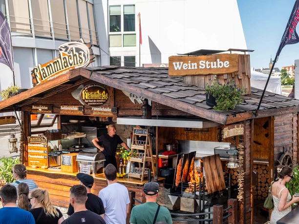 Midsummer festival at the Cologne Chocolate Museum Wooden stand with flame-grilled salmon, fire pit and waiting visitors at a summer festival