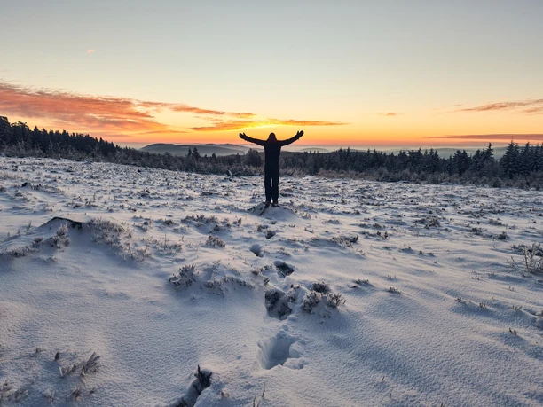 Sonnenuntergang Winterlicht Ein Wanderer steht mit erhobenen Armen in einer Schneelandschaft