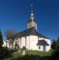 Kirche in Burkhardswalde Weißes Kirchengebäude mit schwarzem Dach und spitzem Turm, umgeben von Gräbern und Bäumen.