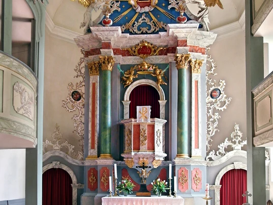 Burkhardswalde Kirche von innen Bunter, kunstvoller Altar mit Säulen, Verzierungen und einem roten Teppich im Kircheninneren.