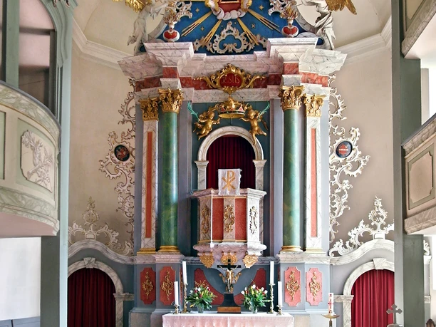 Burkhardswalde Kirche von innen Bunter, kunstvoller Altar mit Säulen, Verzierungen und einem roten Teppich im Kircheninneren.