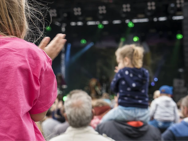Der Familientag in Büsum Eine Menschenmenge vor einer Bühne. Zwei Kinder auf den Schultern von Erwachsenen von hinten.