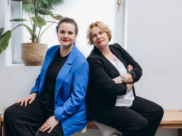 Female-Leadership-Workshop zwei Damen sitzen auf einer Bank vor einer weißen Wand