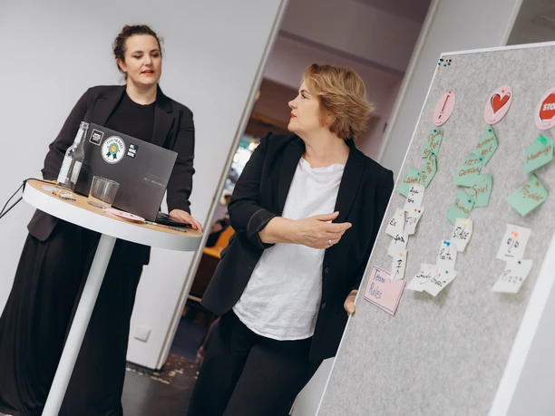 Female-Leadership-Workshop Two people stand at the laptop and presentation board