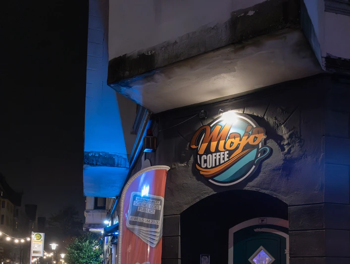07_Mojo-1.jpg Eingang des Mojo Coffee & Diner in Bremerhaven mit leuchtendem Schild und nasser Abendstraße