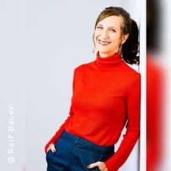 Frau in rotem Rollkragenpullover lächelt und steht vor hellen Hintergrund.
