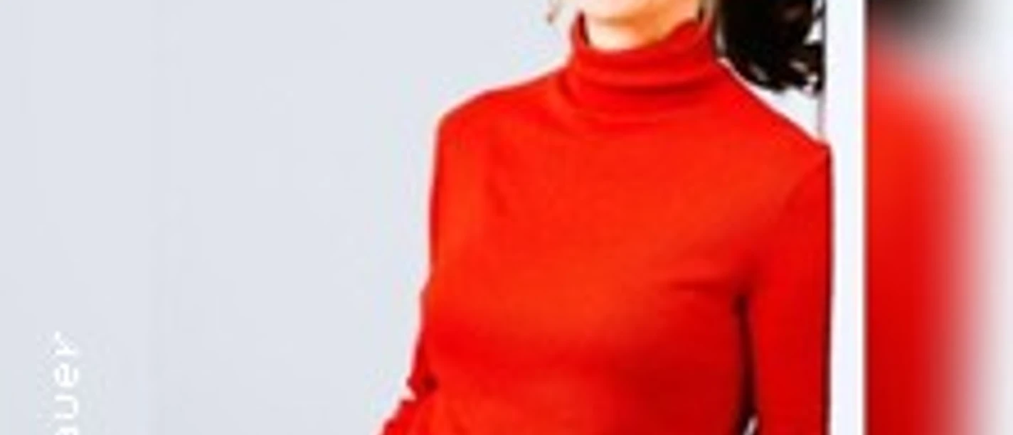Frau in rotem Rollkragenpullover lächelt und steht vor hellen Hintergrund.