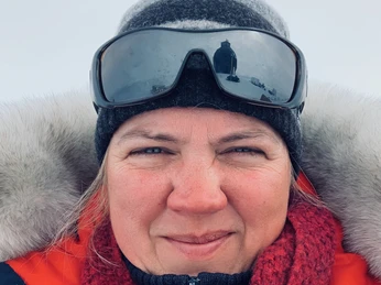 Daniela_Jansen.jpeg Frau mit warmer Winterkleidung und rotem Schal im Schnee, Spiegelung einer Landschaft in Sonnenbrille