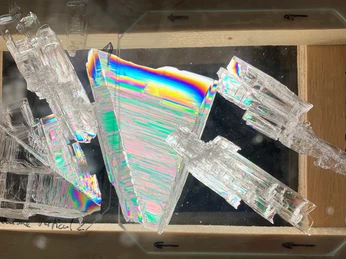 Daniela_Jansen3.jpeg.png Nahaufnahme von schillernden Eiskristallen mit prismatischen Strukturen und regenbogenfarbenen Reflexen.