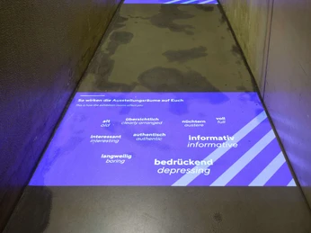 Intervention! How do we tell the history of National Socialism today? Schmaler Flur mit violetter Bodenprojektion, die Begriffe und Eindrücke zur Ausstellung zeigtNarrow corridor with purple floor projection showing concepts and impressions of the exhibition