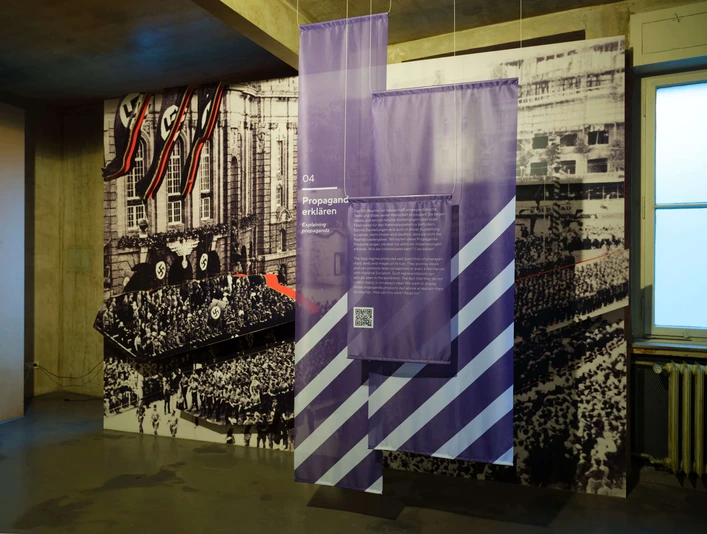 Intervention! How do we tell the history of National Socialism today? Ausstellungsraum mit historischen Propagandafotos und violetten InformationstafelnExhibition room with historical propaganda photos and purple information boards