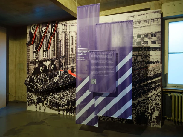 Intervention! Wie erzählen wir NS-Geschichte heute? Ausstellungsraum mit historischen Propagandafotos und violetten Informationstafeln