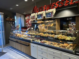 baeckerei-musswessels-Leer-Ceka.jpg Verkaufstheke mit frischen Brötchen, belegten Snacks und Gebäck in moderner Bäckereieinrichtung.